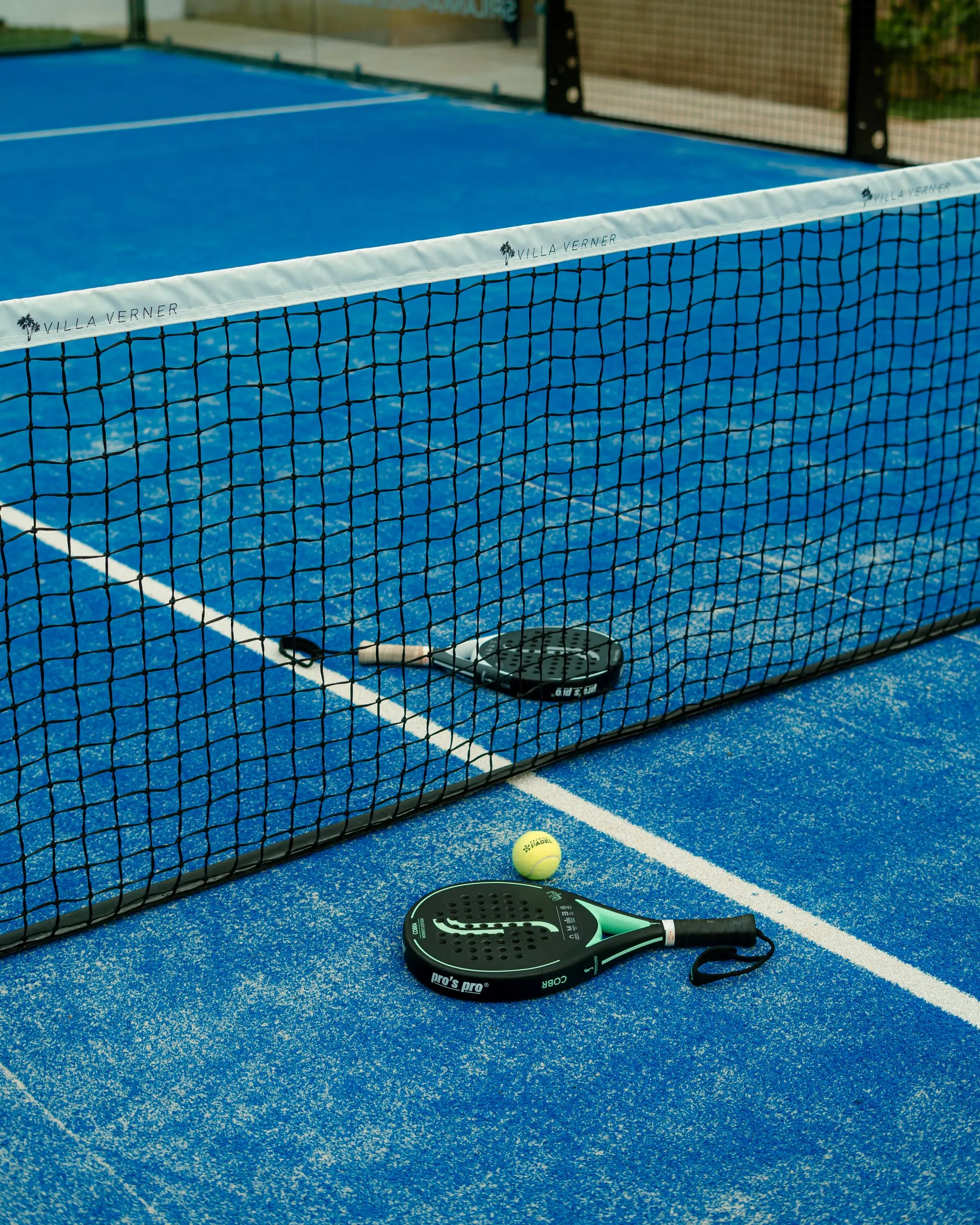 Two padel rackets and a ball on the blue court beside the net