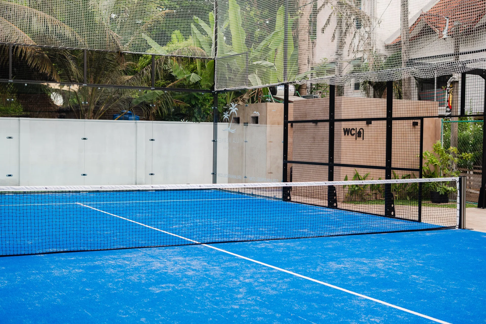 The glass-walled padel court at Villa Verner, palms behind it