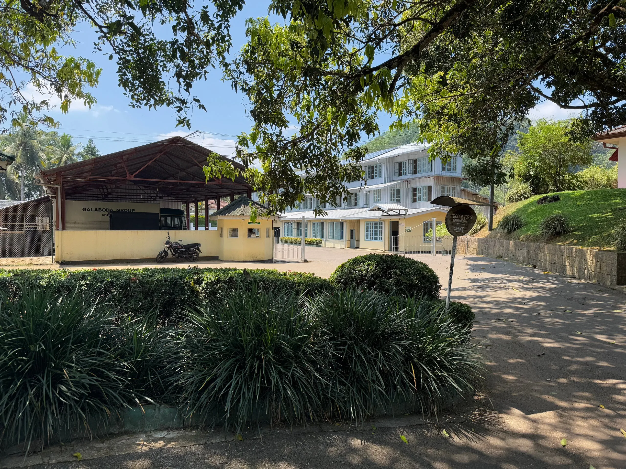 Teevabriku valge hoone Sri Lanka mägede vahel, ees varjualune ja hoolitsetud hekid