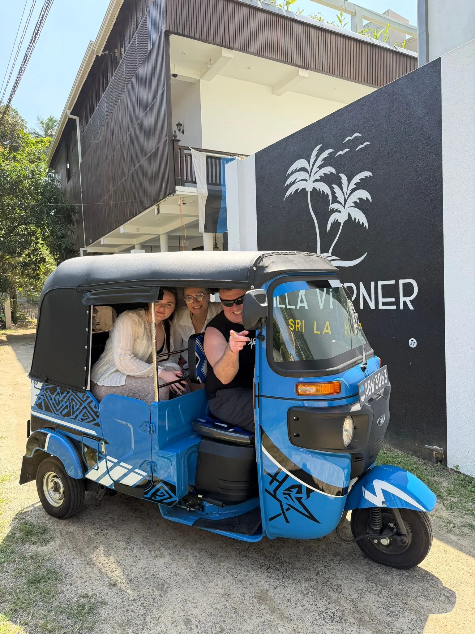 Sinine tuk-tuk villa õuel, taga tumedale seinale maalitud Villa Verneri palmilogo